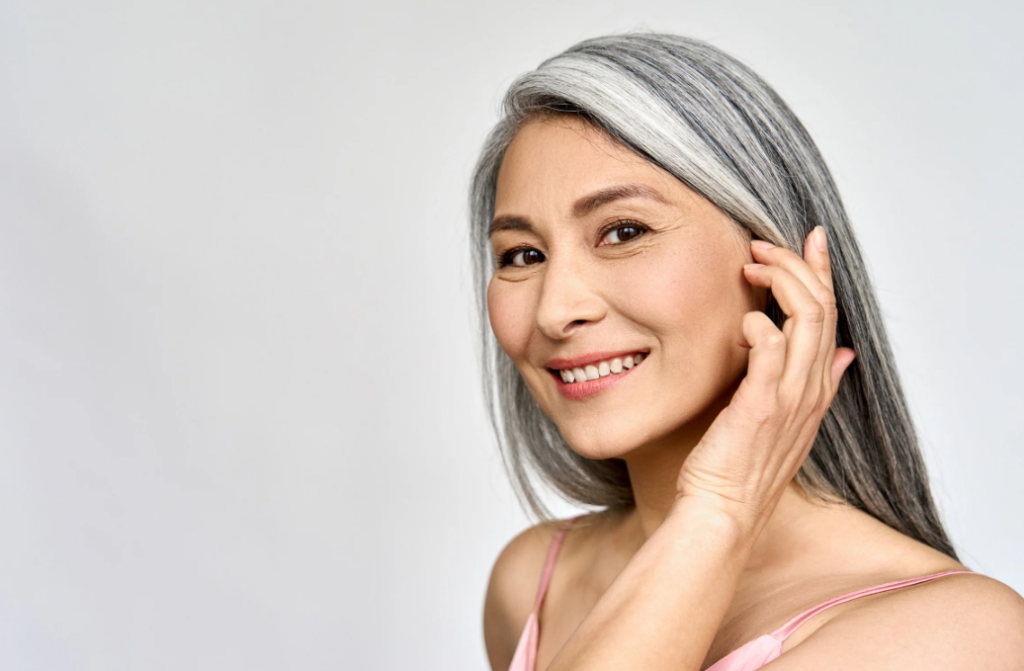 Asian woman with gray hair posing for a photo while showcasing dermal fillers, in this beginners guide.