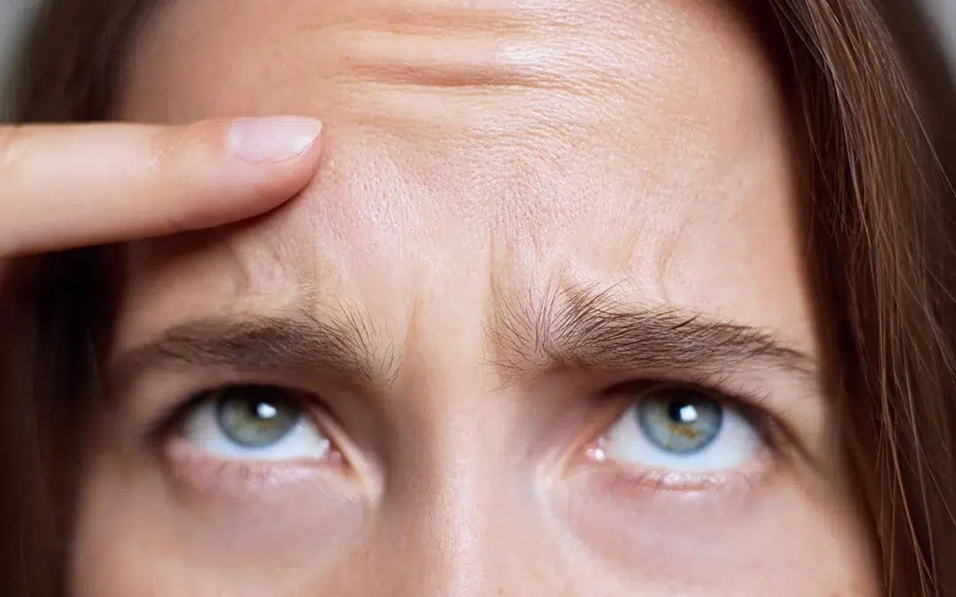 portrait of a woman with light skin and blue green eyes examining forehead wrinkles with a concerned expression