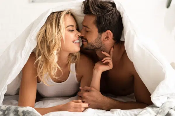 smiling couple going to kiss under sleeping sheets