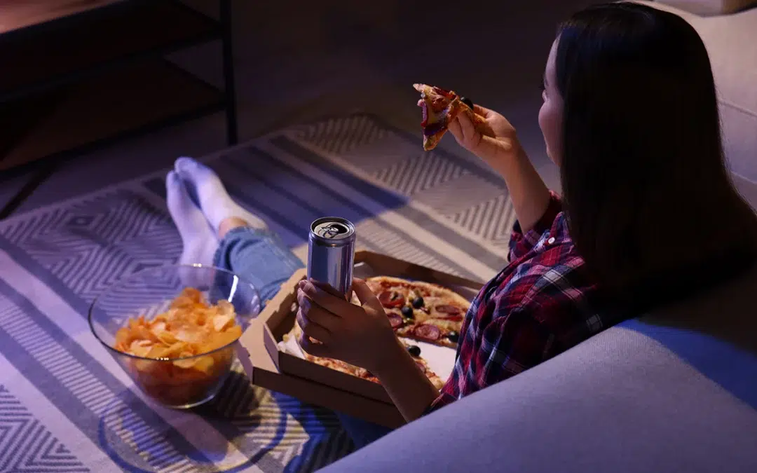 young woman eating pizza while watching tv in room at night