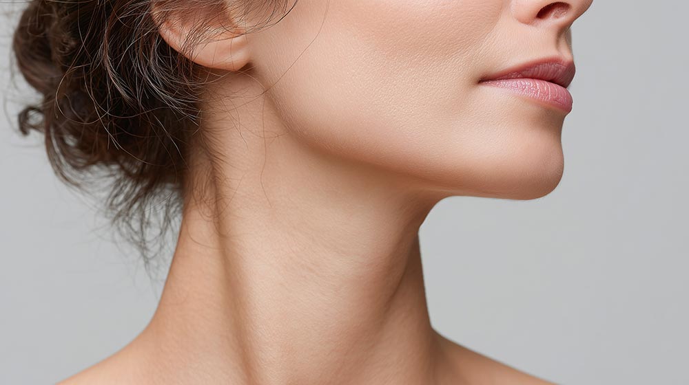Closeup of woman smooth chin line and neck with natural skin tone and soft lighting, showing delicate facial features and calm expression