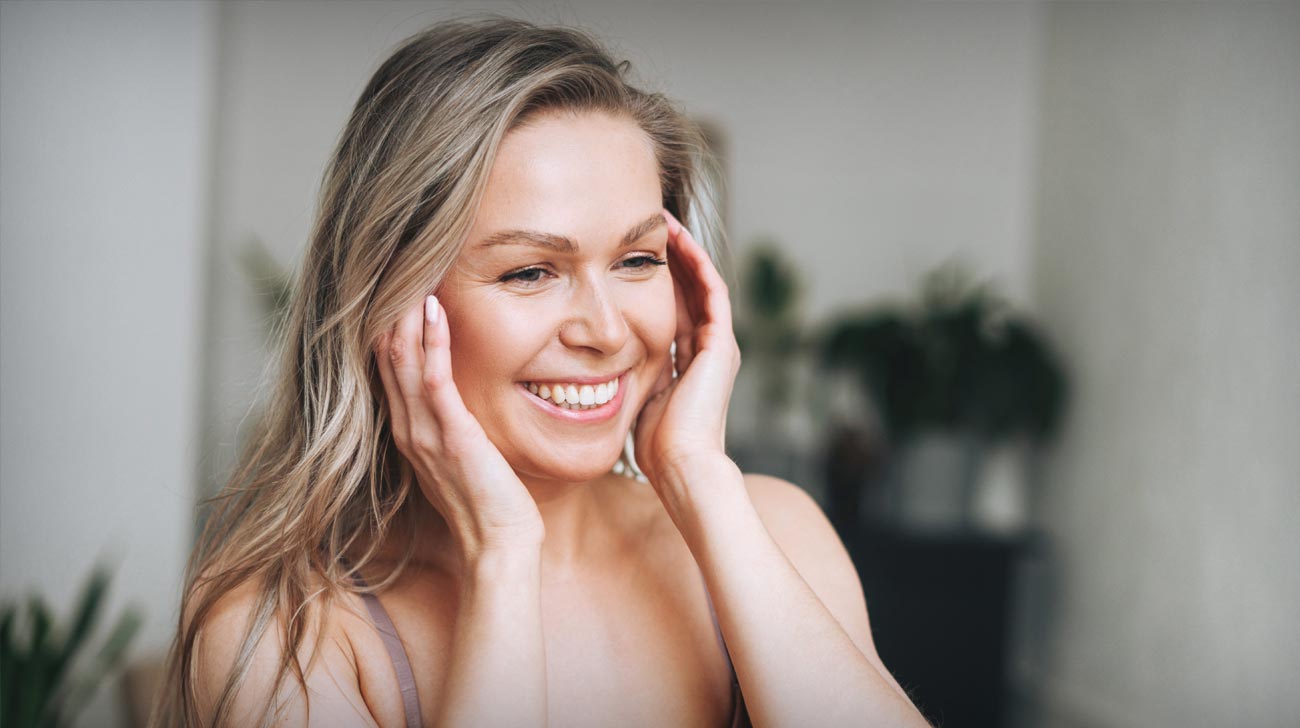 Blonde smiling woman with long hair does facial massage in underwear at bathroom, banner