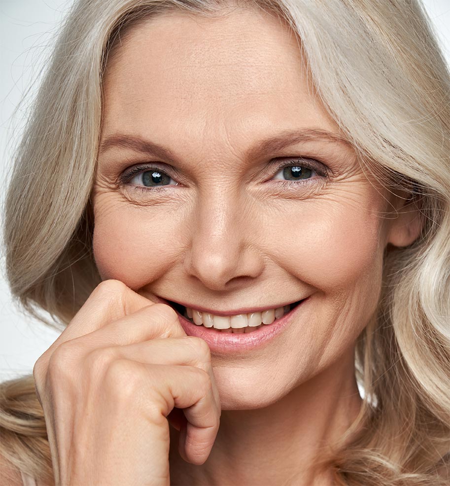 Happy pretty 50s middle aged woman touching healthy soft face skin, smiling, looking at camera.