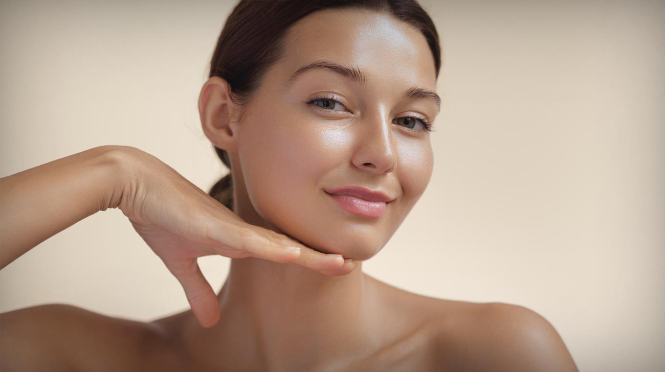 Happy beautiful young adult woman touching her perfect face with healthy shiny skin, hand on chin.