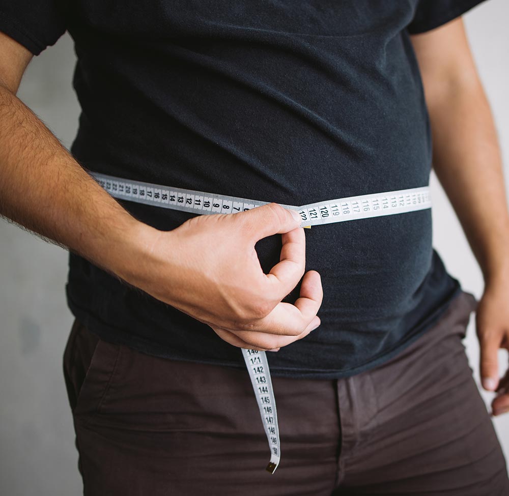 Overweight man measuring waist with measure tape, close up image. Weight loss, motivation, fat burning