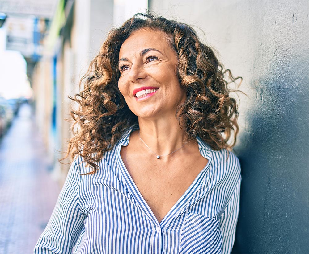 Middle age hispanic woman smiling happy leaning on the wall at the city.