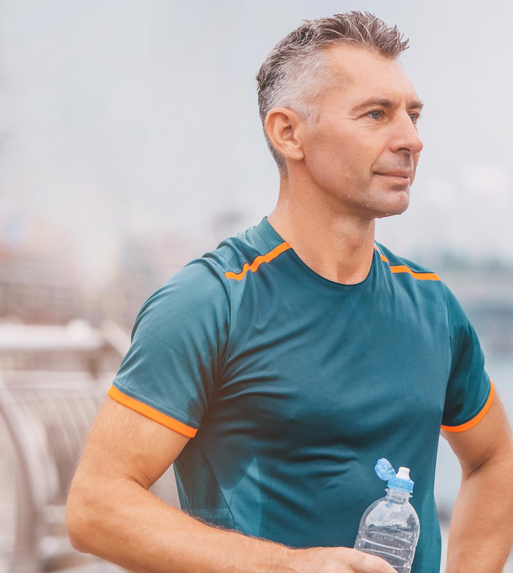 Portrait of healthy athletic middle aged man with fit body holding bottle of refreshing water, resting after workout or running.