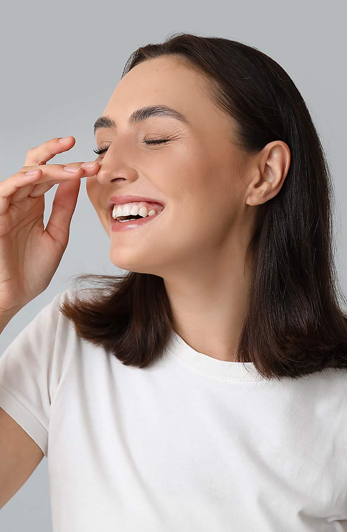 Young woman touching her nose on light background, closeup