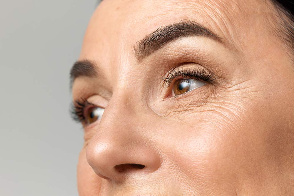 Cropped portarit of beautiful middle-aged woman with healthy, natural condition skin looking away over grey studio background.